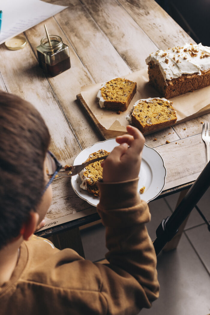 Child eating a cozy butternut squash autumn cake slice with frosting on a white plate at a wooden table.