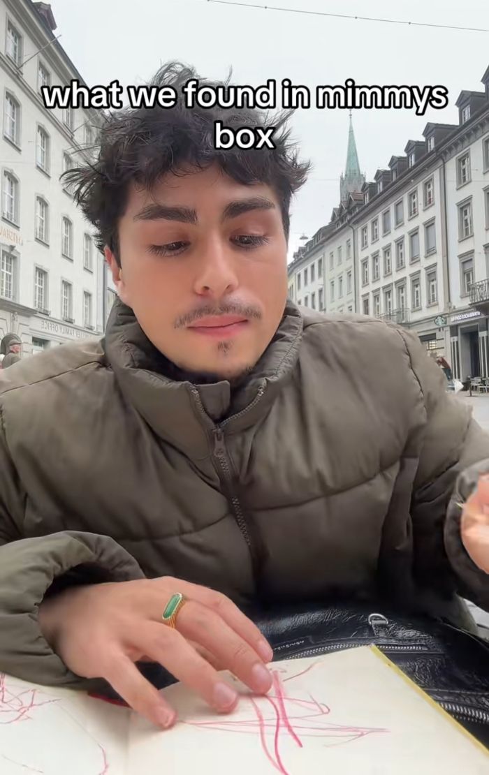 Man in Europe examining mysterious lockbox contents left by grandmother while sitting at outdoor cafe table.