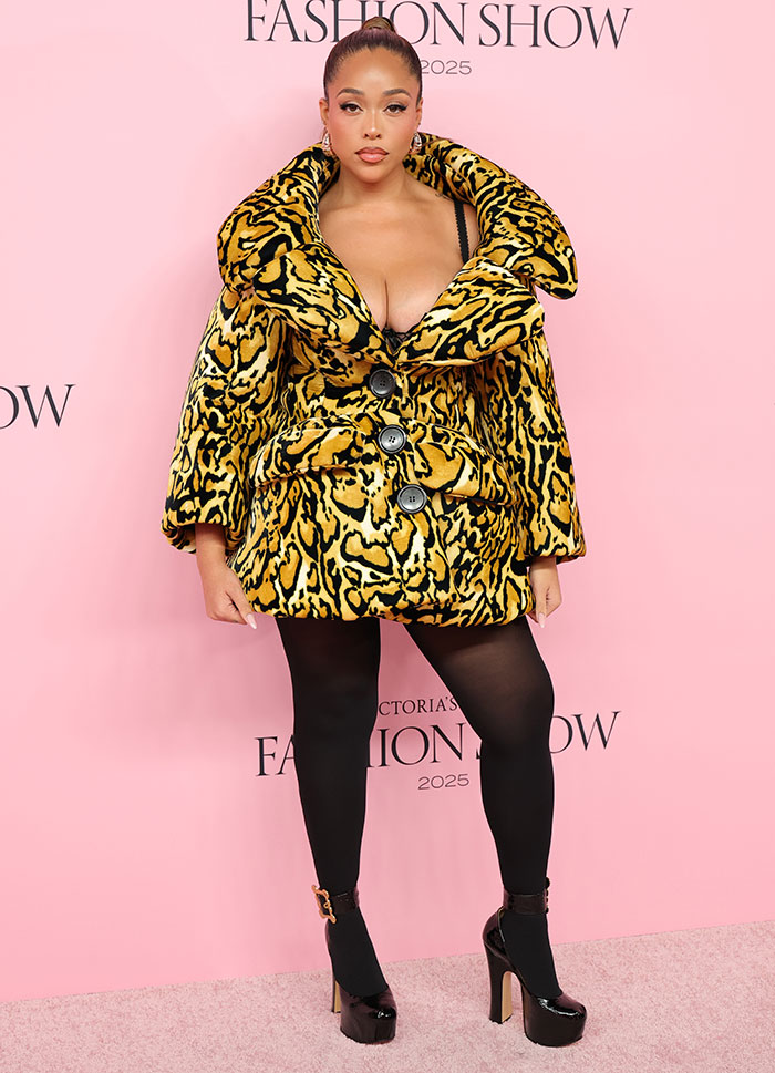 Woman in bold animal print coat and black tights posing at Victoria's Secret Fashion Show 2025 with risqué looks.