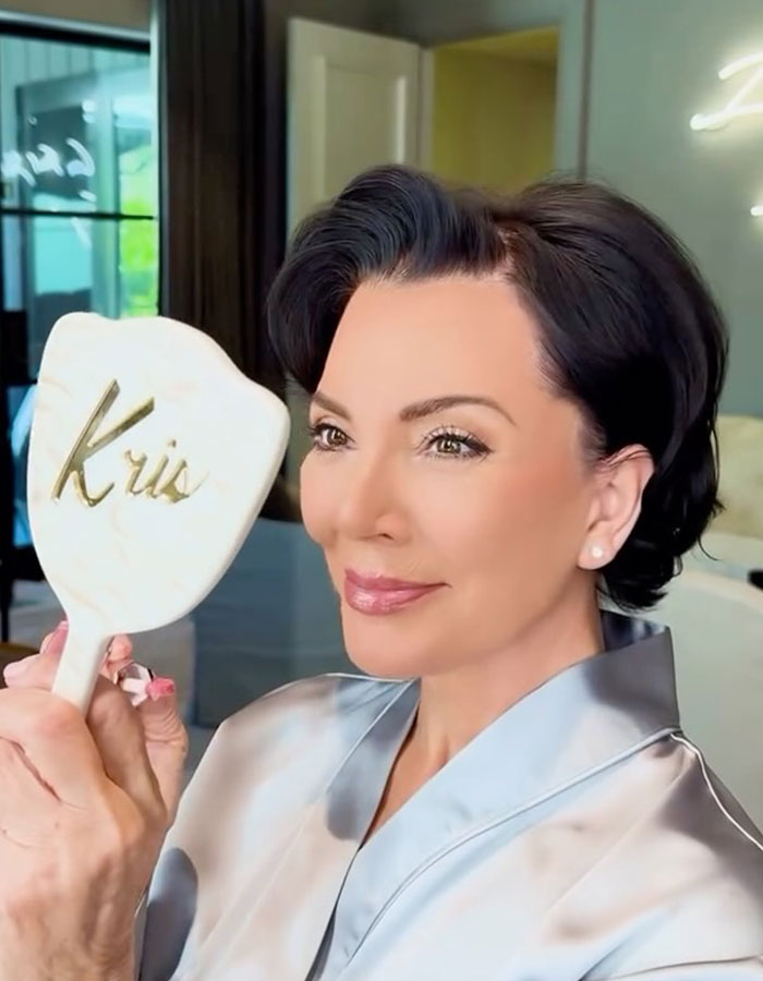 Kris Jenner in a silky robe holding a personalized mirror, showcasing her latest public appearance and style update.