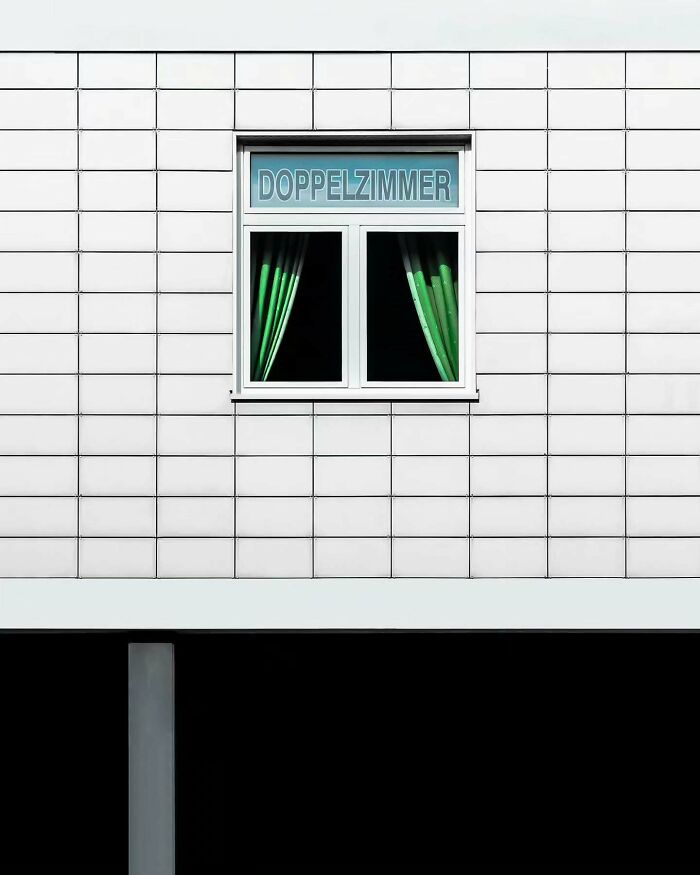 Minimalist architectural vision shown in a white tiled building facade with a single window and green curtains.