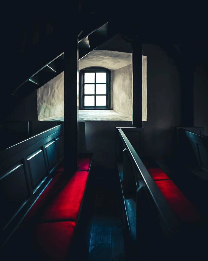 Dark minimalist interior with wooden benches featuring red cushions and natural light from a single window in architectural space