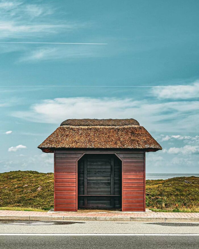 Minimalist architectural vision showcased in a simple wooden shelter with a thatched roof by the roadside under a clear sky.