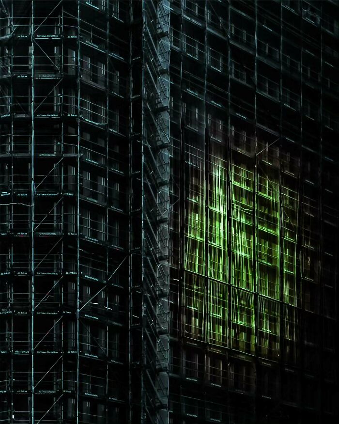 Minimalist architectural design featuring dark glass facade with illuminated green window details at night.
