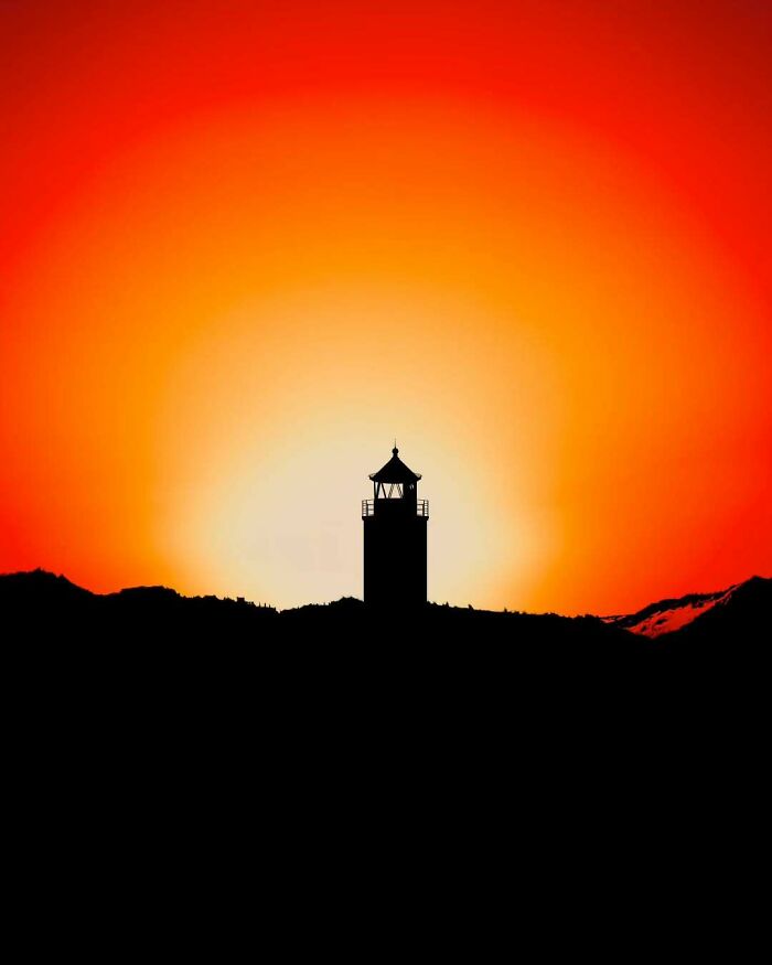 Silhouette of minimalist architectural lighthouse against a vibrant orange sunset sky, highlighting minimalist architectural vision.