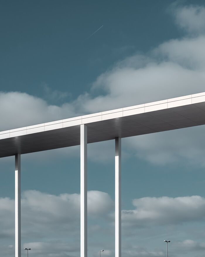 Minimalist architectural structure with clean lines and tall white pillars under a cloudy blue sky.