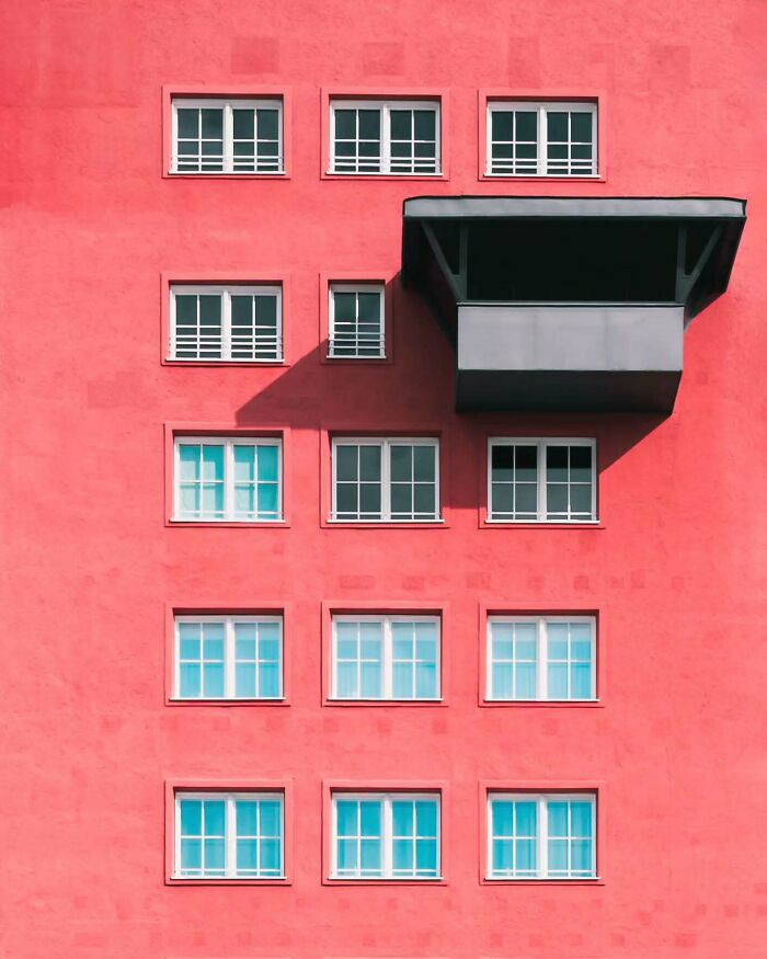 Minimalist architectural design featuring a bright coral building facade with symmetrical windows and a black balcony.