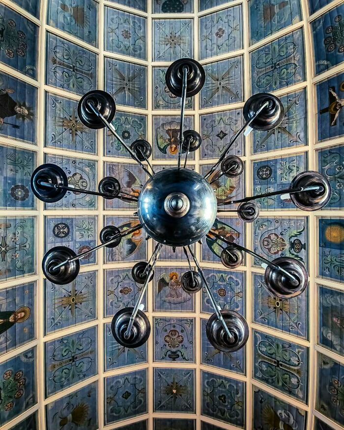 Minimalist architectural chandelier design in a detailed ceiling with painted floral and angel motifs.