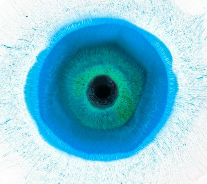 Close-up image of hypnotic ink and water art resembling a detailed human eye with vibrant blue and green hues.