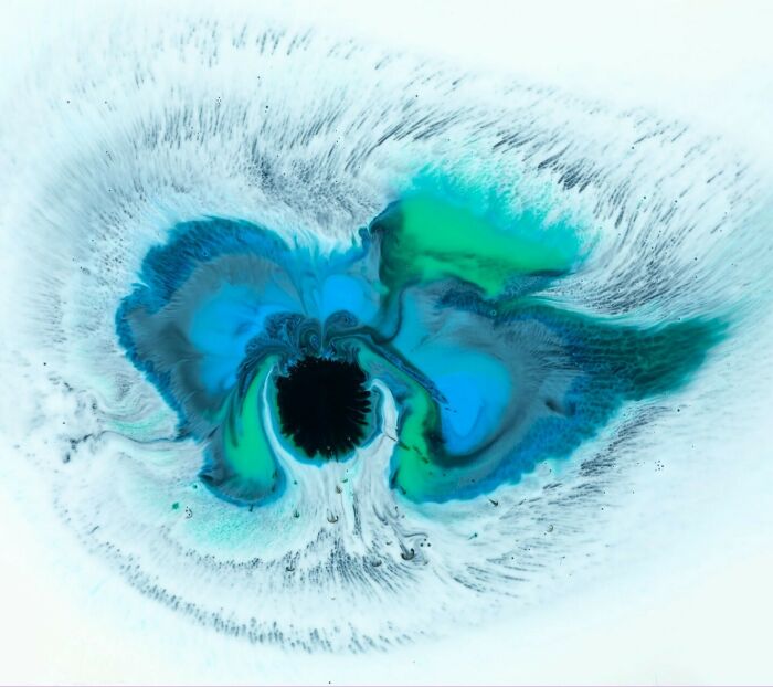 Abstract ink and water image resembling a hypnotic human eye with swirling blue and green colors and a dark center.