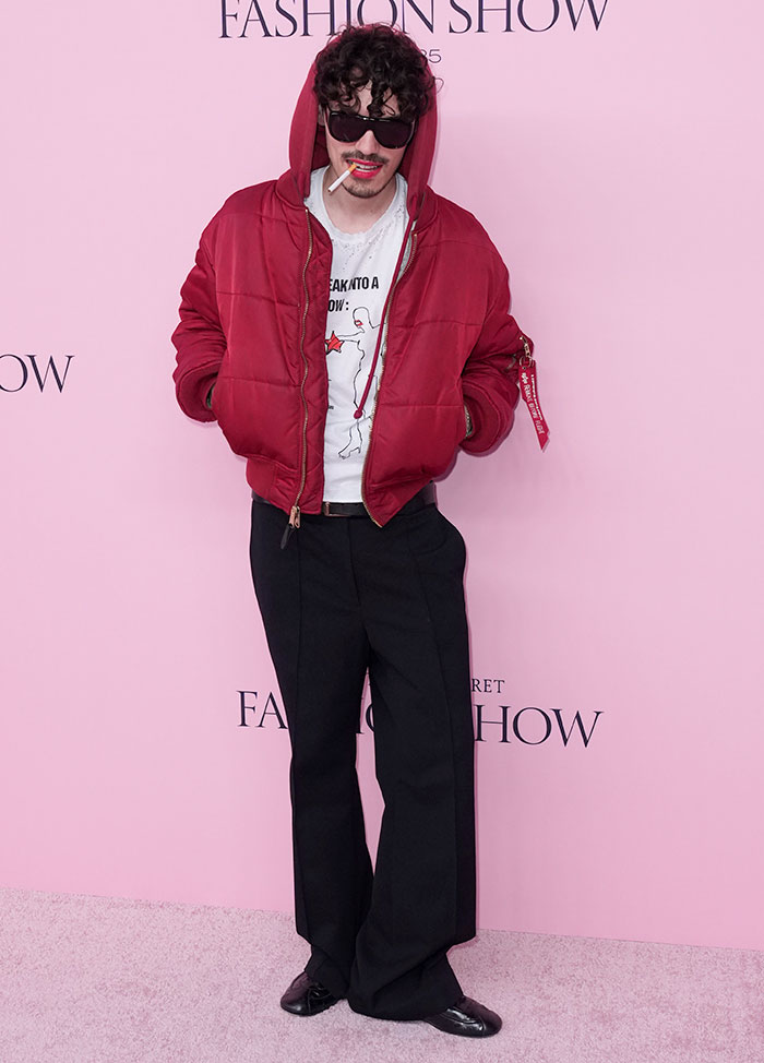Man in oversized red jacket and black pants posing at Victoria's Secret Fashion Show 2025 worst dressed risqué looks event.
