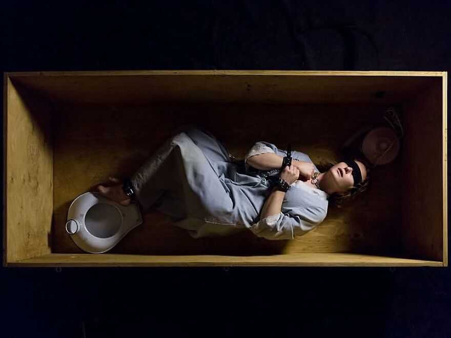 Woman in a prison uniform lying blindfolded and handcuffed inside a wooden box, depicting movies based on true stories.
