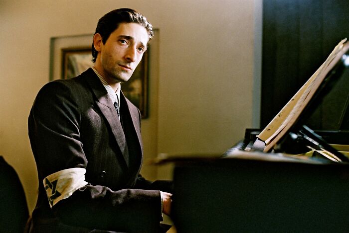 Actor dressed in period clothing playing piano in a dramatic scene from movies based on true stories.