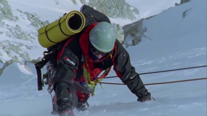 Climber wearing helmet and carrying gear ascending icy mountain in scenes from movies based on true stories.