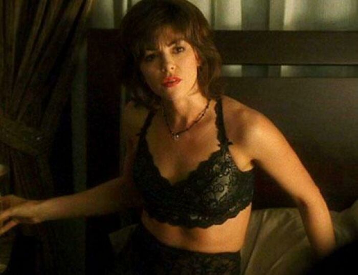 Woman in a black lace bra sitting on a bed, representing unrealistic women movie tropes in film scenes.