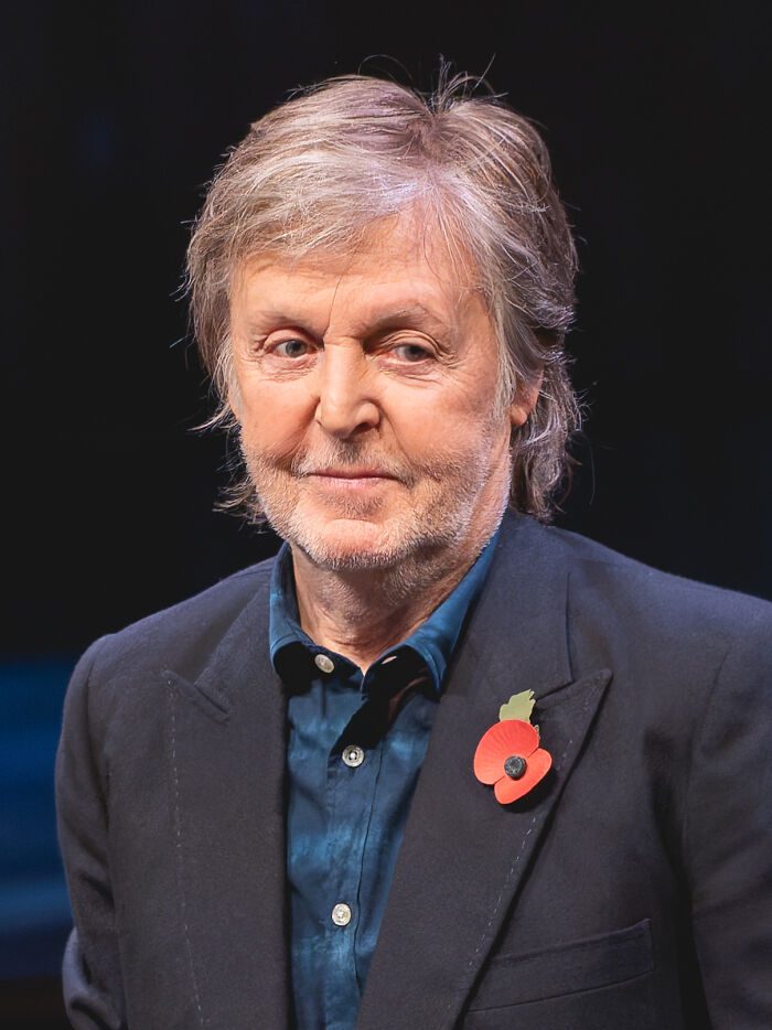 Older man with gray hair and beard, wearing a dark blazer with a red poppy pin, linked to unknown things about celebrities.
