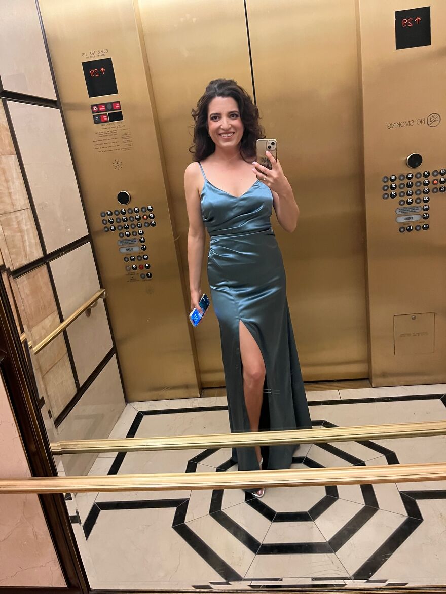 Woman in a long satin dress taking a selfie in an elevator after launching billboard campaign to find love