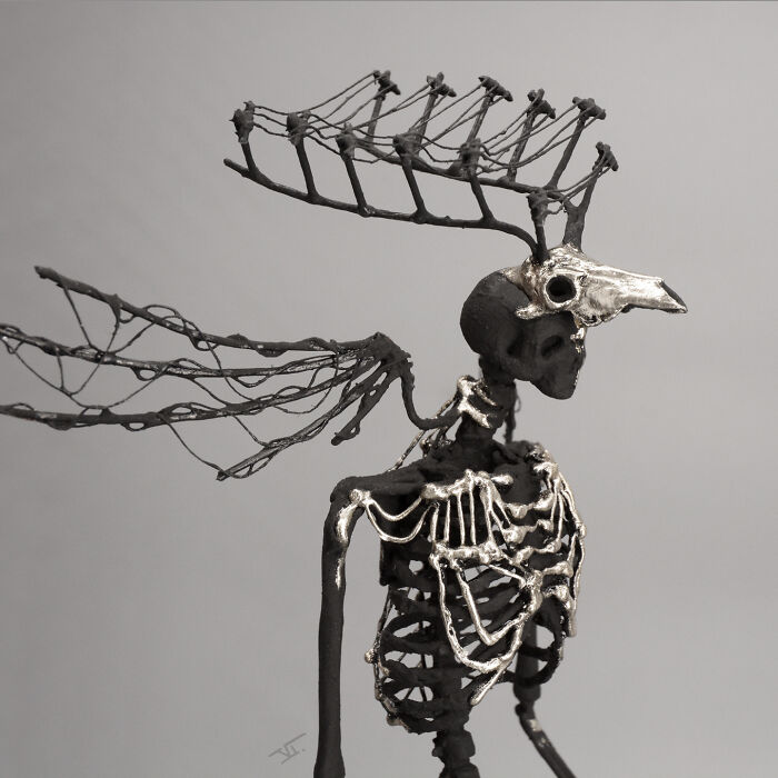 Haunting porcelain sculpture of a skeletal figure with bird skull mask and intricate wing-like structures against a plain background.
