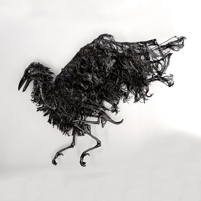 Haunting porcelain sculpture of a dark, tattered bird resembling relics of forgotten myths with intricate, eerie details.