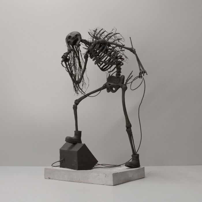 Haunting porcelain sculpture of a skeletal figure with long hair holding a microphone, evoking relics of forgotten myths.