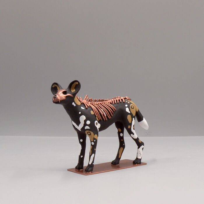 Porcelain sculpture of a stylized animal with haunting skeletal details and myth-inspired painted patterns on a plain background.