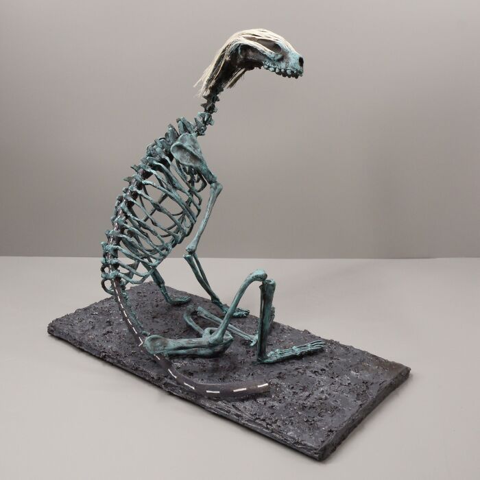 Haunting porcelain sculpture resembling an ancient mythical creature skeleton on a textured dark base.