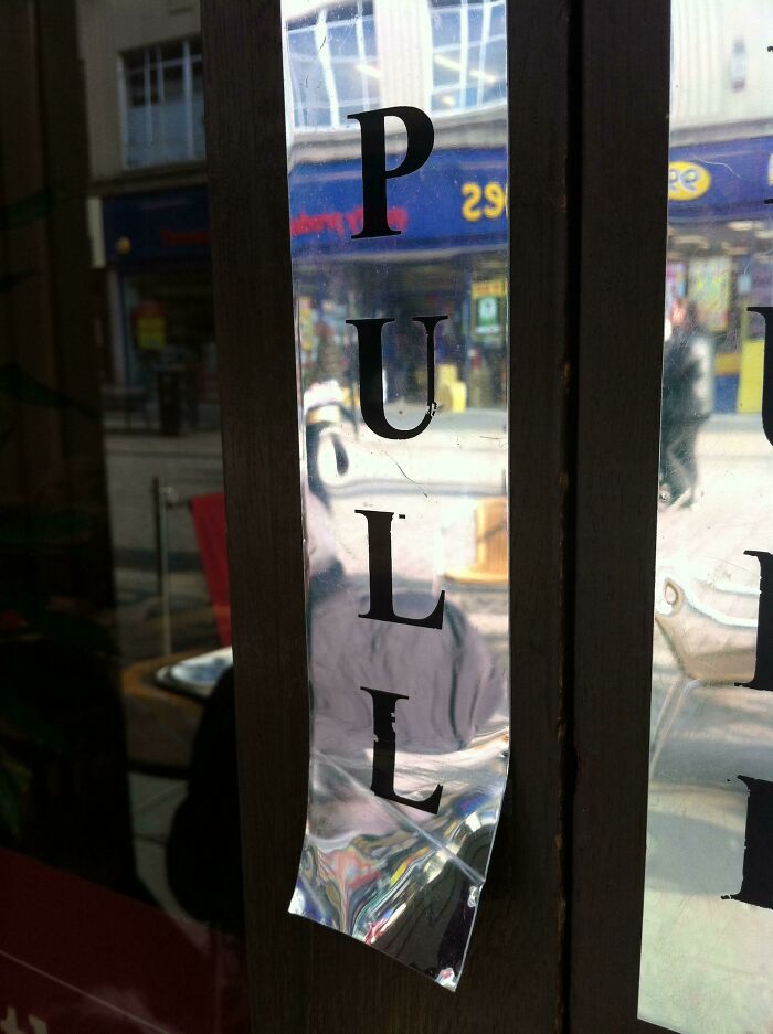Distorted pull sign on glass door, showing an unhinged way of people doing exactly what they were asked to do.