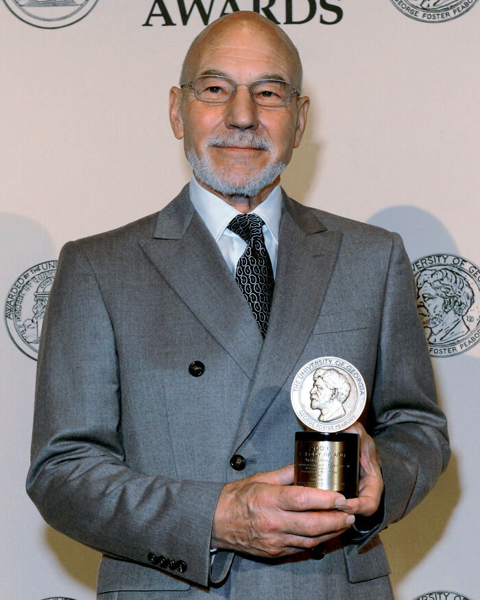 Older male Hollywood star in gray suit holding an award, representing stars who found fame after 30.