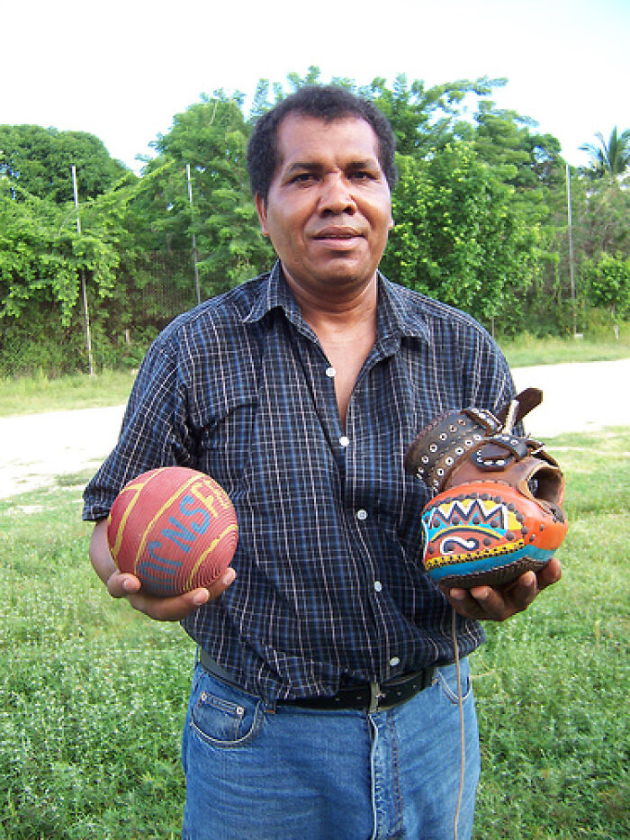 Man outdoors holding a decorated ball and a spiked leather glove representing dangerous historical sports equipment.