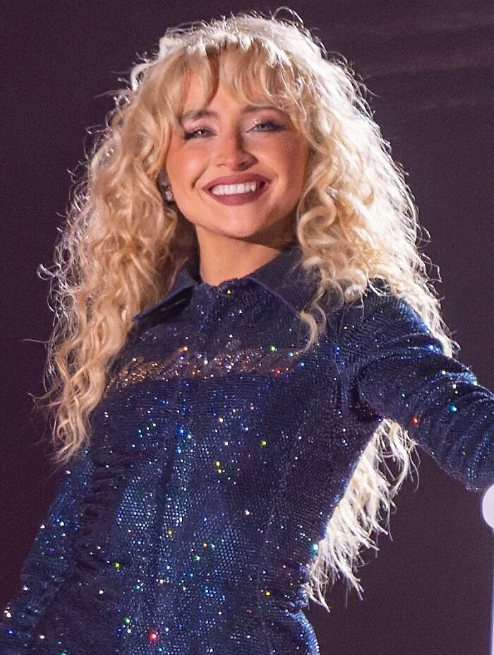 Blonde woman with curly hair wearing a sparkly blue outfit smiling on stage, representing celebs people can't stand.