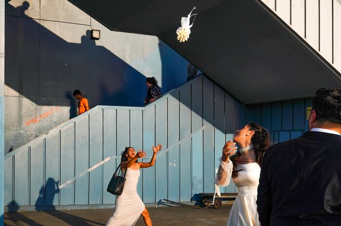 Two women in white dresses catching a bouquet on the street, captured in a dynamic pure street photography moment.