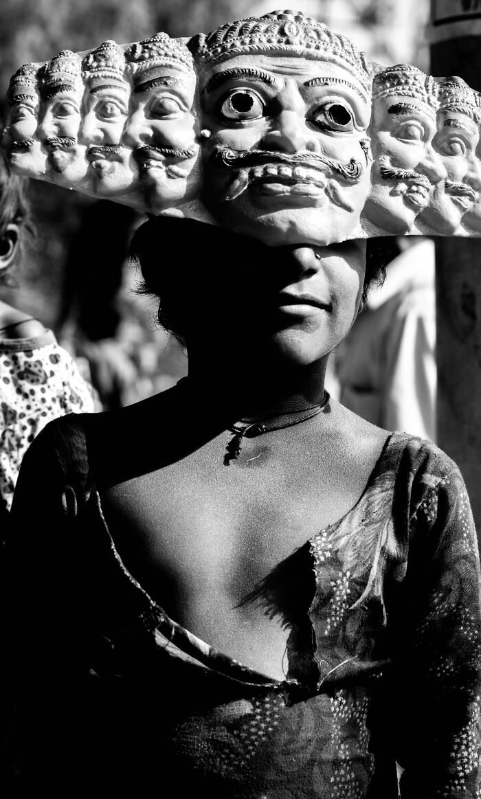 Black and white street photography of a person wearing a multi-faced traditional mask in pure street photography awards.