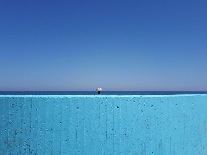 Minimalist street scene featuring a blue wall and solitary figure under clear sky, showcasing pure street photography awards style.
