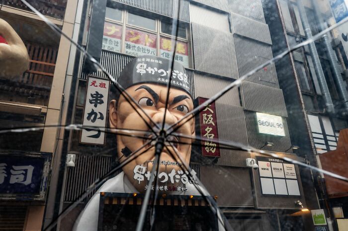 View through c*****d glass of a street scene featuring large Japanese statue and urban signs, showcasing pure street photography awards.