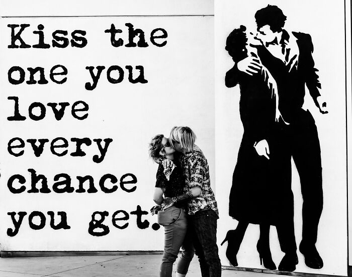 Couple kissing in front of street art with love message, captured in a black and white pure street photography awards image.