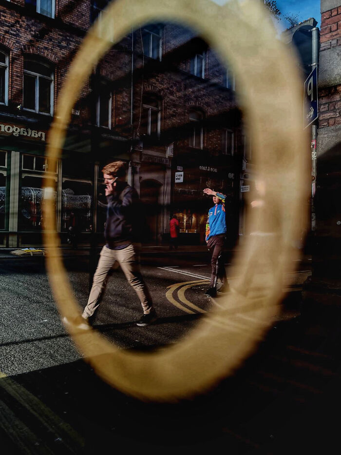 Street photography showing pedestrians crossing a city street reflected through a circular window frame.