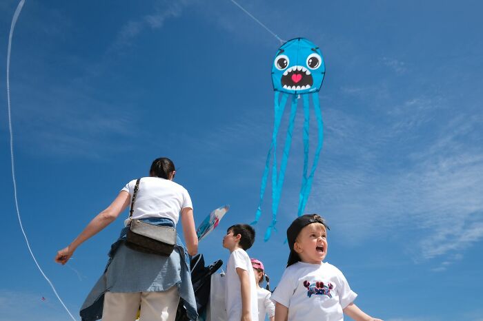 Children and an adult flying a blue octopus kite under a clear sky in a pure street photography awards scene.
