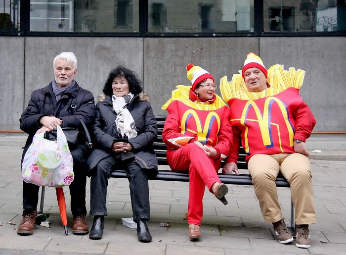 Two elderly people sitting next to two people dressed in McDonald's fries costumes in a street scene for street photography awards.
