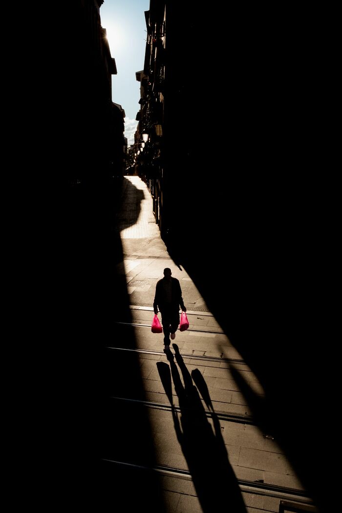 Silhouetted person walking with pink bags on a street, showcasing pure street photography capturing urban shadows.