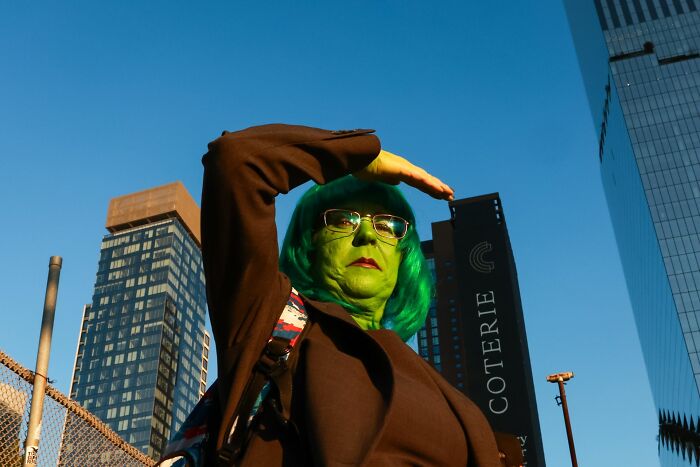 Person with green face paint and green wig posing in an urban setting for pure street photography awards image.