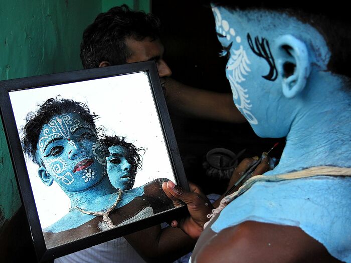Person with blue face paint looking into a mirror, capturing the essence of pure street photography awards.