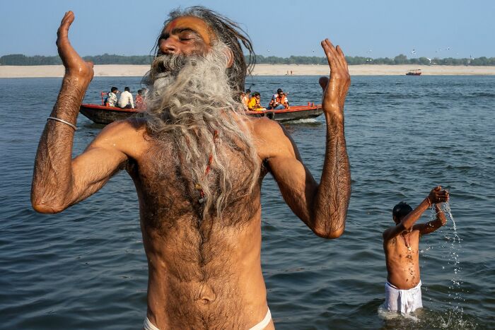 Elderly man with long beard and raised arms bathing in river, capturing pure street photography awards street life moment.