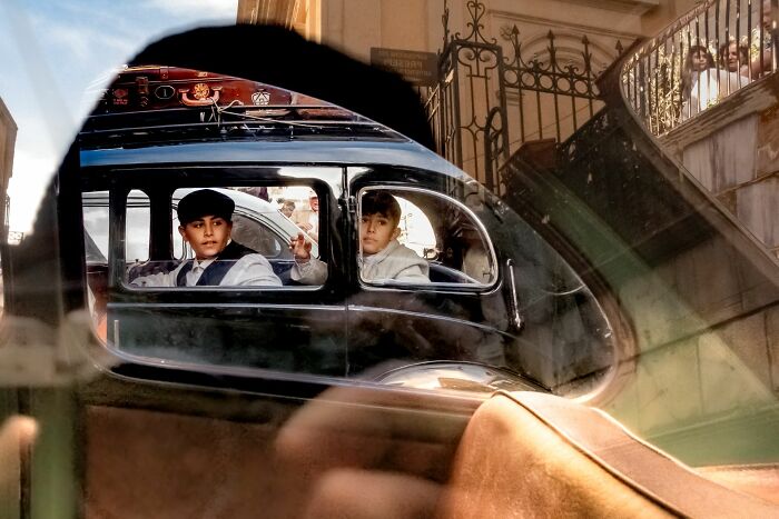 Two boys in vintage car, captured through window reflection, exemplifying pure street photography award winning moment.