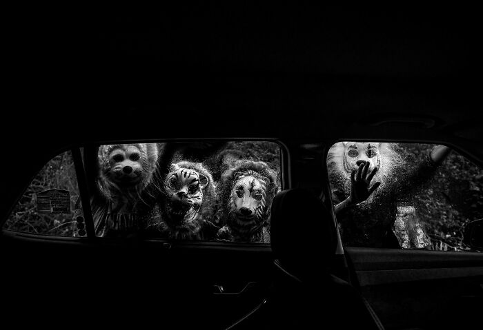 Four eerie figures in animal masks outside a car window captured in a striking black and white pure street photography scene.