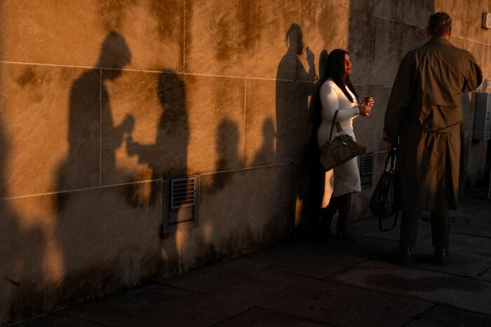 Shadows of people cast on a wall during golden hour, capturing candid moments in street photography.