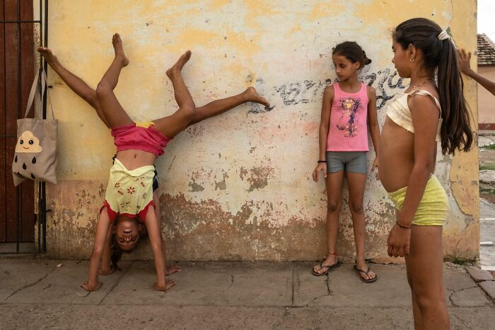 Three children playing near a worn wall, captured in a candid moment for Pure Street Photography Awards 2025.