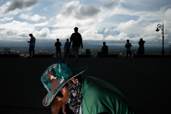 Person in a camouflage hat and bandana captured in dramatic light, showcasing street photography's raw and candid moments.