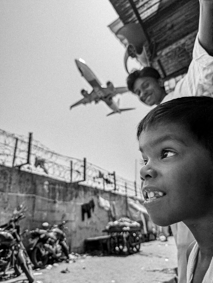 Black and white street photography of children with a low-flying airplane, capturing the soul of the streets in a candid moment.