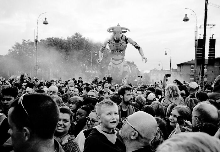 Crowd gathered outdoors around large mechanical bull figure in black and white street photography scene.
