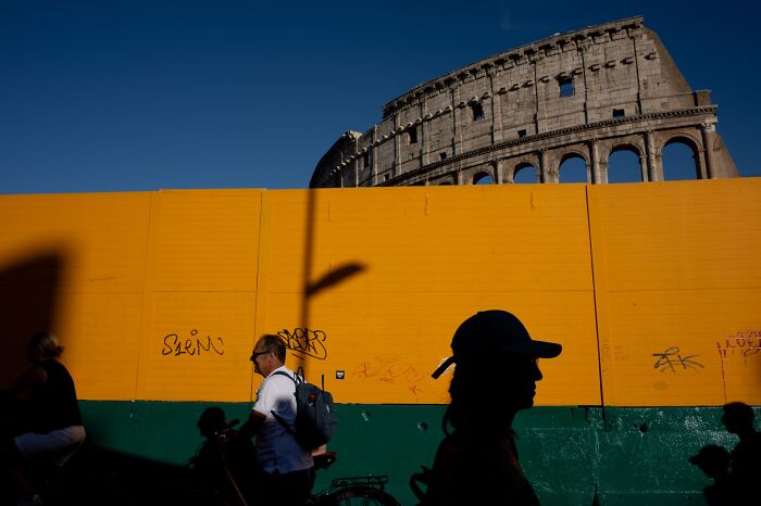 Silhouettes of pedestrians passing colorful wall with graffiti near ancient Roman Colosseum in street photography.